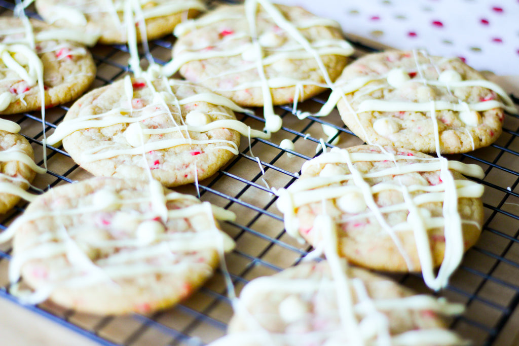 cookies with white chocolate chips and peppermint pieces covered in white chocolate drizzle sitting on a cooling rack