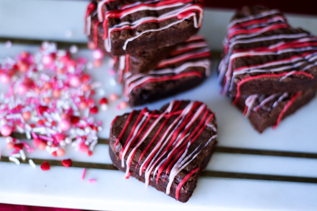 heart shaped brownies with red and pink drizzle on a white board with valentine sprinkles on the left